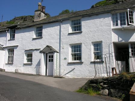 A white row house with multiple windows and a white door along a paved street at White Lion Cottage in Chapel Stile
