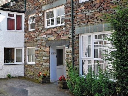 Stone and white painted exterior walls with multiple windows and a white door with plants and flowers at Low Croft Cottage in Grasmere