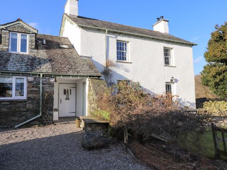 The exterior of a stone and white plaster house with a gravel driveway and outdoor seating at Robin Cottage in Troutbeck
