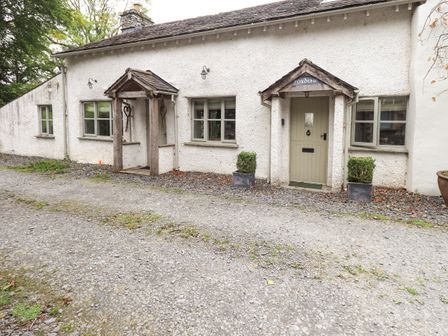 Exterior view of a white textured cottage with two wooden porches and gravel driveway at Foxdene Cottage in Underbarrow