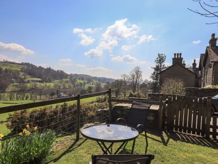 A garden area with a round glass table and chairs overlooking green hills and trees at Boxwood Cottage in Troutbeck