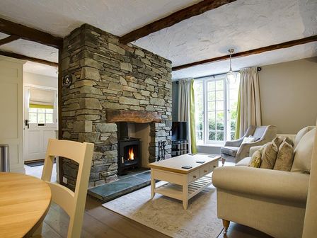 A living room with a stone fireplace a coffee table two armchairs and a sofa at Acorn Cottage in Grasmere