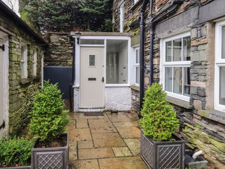 A stone exterior courtyard with a white door and potted plants at Wainwright Cottage in Ambleside