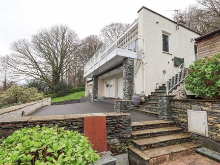 The exterior of a two-story house with stone steps and columns surrounded by trees and greenery at Tanna Hill in Bowness