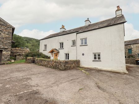 A white farmhouse with stone walls and a small wooden porch in a rural setting at Satterthwaite Farmhouse - Sleep 8 in Grizedale