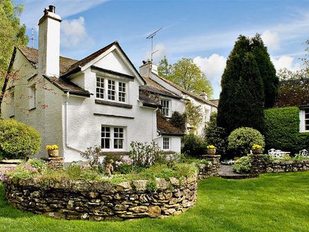 A white house with a stone flower bed and green lawn at High Cleabarrow in Windermere