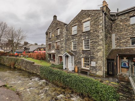 Stone buildings next to a river with a stone wall and hedges at Idle Mill 2 in Ambleside