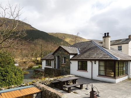 A cottage with a stone wall picnic table and benches outside near hills at Thirlmere Cottage in Grasmere