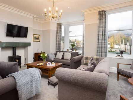 A living room with sofas a wooden coffee table a fireplace and windows with plaid curtains at Thirty Blencathra Street Keswick