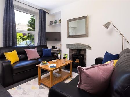 A living room with black leather sofas and colorful cushions a wooden coffee table and a fireplace at Fell Cottage Ambleside
