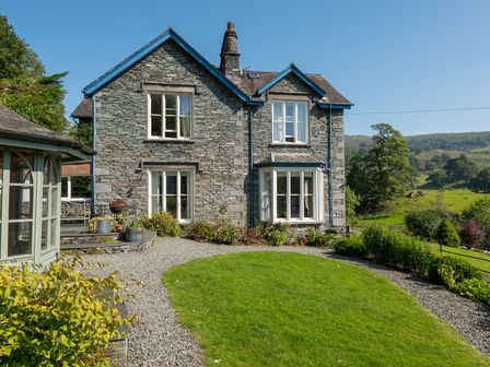 A stone house with blue trim surrounded by a gravel path and green lawn at Stepping Stones House in Ambleside