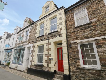 A street view of stone and brick houses with a red door and shopfronts in Mevagissey
