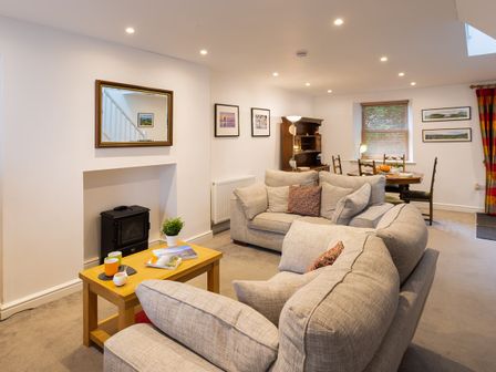 A living room with sofas a wooden coffee table a small black stove a mirror and framed pictures at Fern Cottage in Ambleside