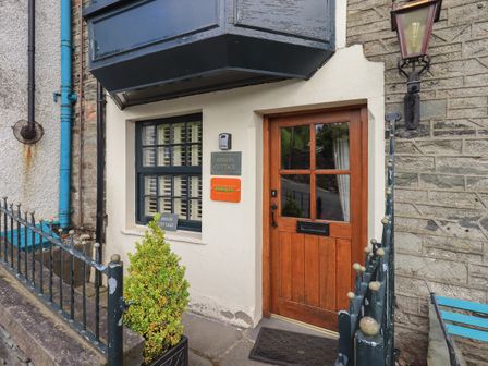 Entrance to a cottage with a wooden door a black metal railing and a small green bush at Heron Cottage in Ambleside