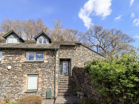 A stone house with two dormer windows and stairs leading to a door with surrounding bushes and trees at Oak Bank in Ambleside