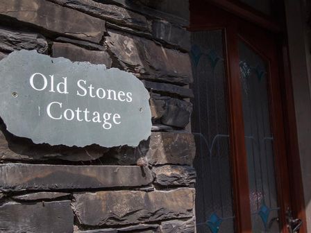 A stone wall with a sign reading Old Stones Cottage next to a wooden door with stained glass windows at Old Stones Cottage in Ambleside
