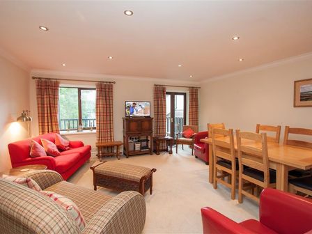 A living room with red sofas wooden dining table and chairs a TV on a wooden cabinet and plaid curtains at The Miller in Ambleside