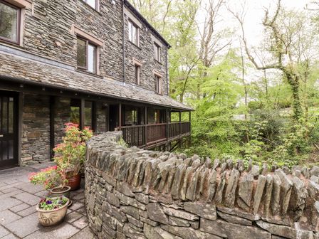 A stone building with wooden balcony and potted plants next to a stone wall and trees outside at Waterfalls in Ambleside