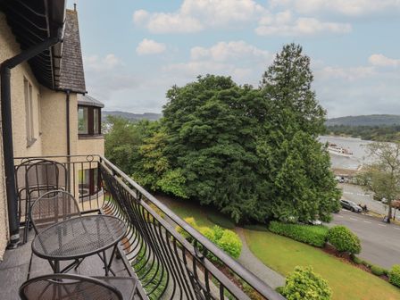 A balcony with black metal table and chairs overlooking trees a river and a road at Romney 17 in Ambleside