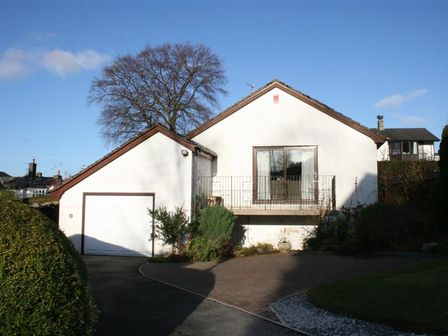 A white single-story house with a garage and balcony surrounded by shrubs and trees at Todd Crag in Ambleside