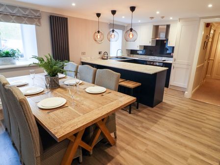 A dining table set with plates and glasses beside a kitchen island with hanging lights at Leafy Nook in Ambleside
