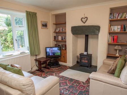A living room with two cream sofas a wood burning stove a television and bookshelves at Sunset Cottage in Ambleside