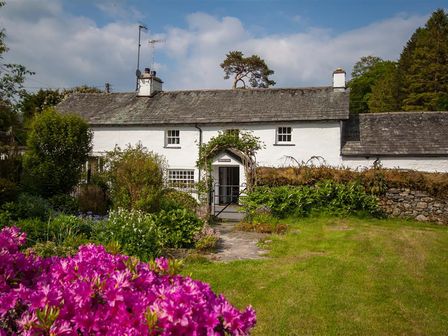 A white cottage with a slate roof surrounded by a garden with flowers and greenery at The Old Farm in Skelwith Fold