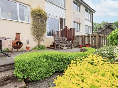 A garden patio with wooden bench chiminea orange chairs stone steps and trimmed hedges at Fellcroft in Troutbeck