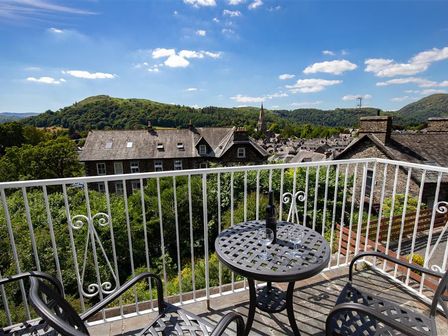 A balcony with a metal table and chairs overlooking houses and hills at Top Notch in Ambleside