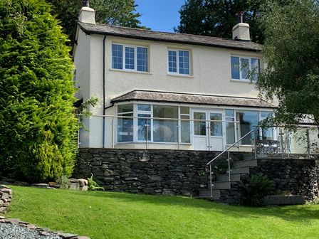 A two-story house with white walls and multiple windows overlooking a lawn with stone steps and glass railing at Gale Mews Ambleside