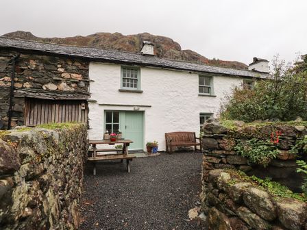 A stone cottage with a green door and windows with outdoor bench and table with flowers at Middlefell Farm Cottage in Great Langdale