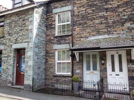 Front of a stone house with two white doors and a brown door with metal fences in front at Acorn Cottage Ambleside