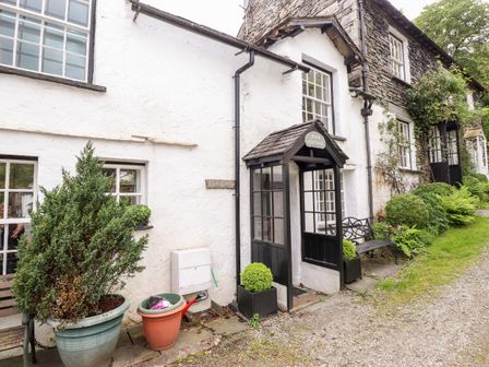 The front entrance of a white cottage with black framed door and windows surrounded by plants and shrubs at Rock Cottage Ambleside