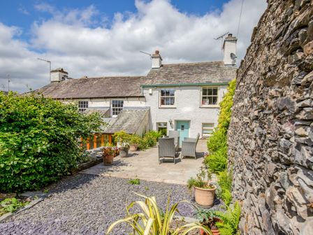 An outdoor patio area with chairs and plants beside a stone wall and white house at Highfold in Ambleside