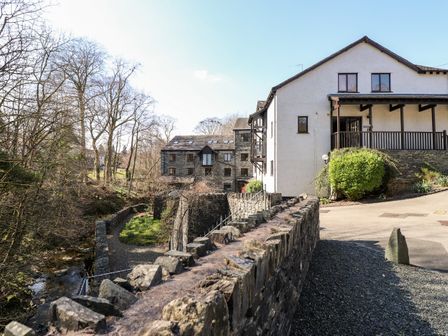 A stone bridge over a small stream with buildings and leafless trees in the background at Ghyll View in Ambleside