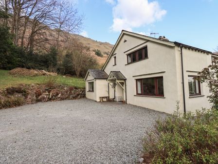 A two-story cream house with gravel driveway and surrounding greenery at Rawfell in Great Langdale