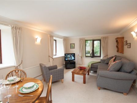A living room with a gray sofa and armchair a wooden coffee table a small dining table with place settings and a television at Over Ghyll in Ambleside