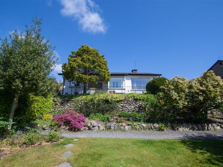 A house with a garden and stone wall under a blue sky at Bield How in Ambleside