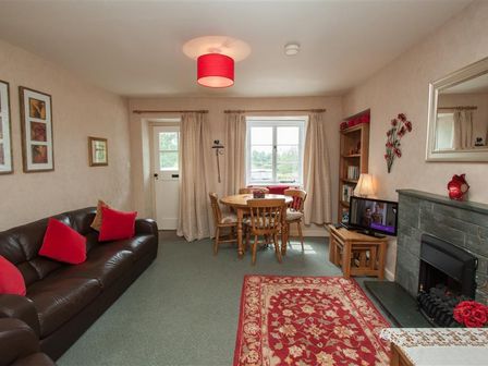 A living room with a brown leather sofa with red cushions a wooden dining table and chairs and a fireplace at Honeypot Cottage in Ambleside