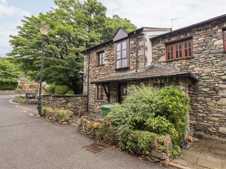 A stone cottage with plants outside next to a streetlamp on a road bend at Chapelside Cottage in Ambleside