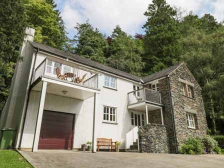 A two story house with white and stone exterior a garage a bench and two balconies surrounded by trees at Orchard House in Ambleside
