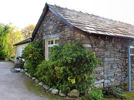 A stone house with a tiled roof and green bushes along the side at Bank Foot in Ambleside
