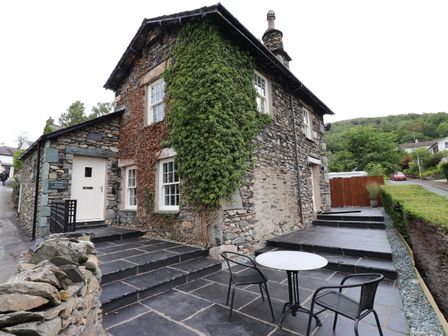 A stone cottage with ivy on the walls and a small patio with table and chairs at Fisherbeck Farm Cottage Ambleside