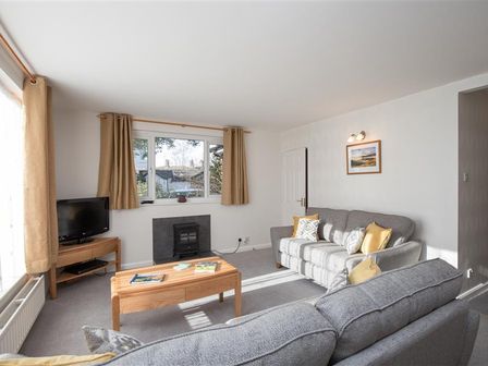 A living room with two gray sofas a wooden coffee table a television on a wooden stand and beige curtains at Yew Tree Cottage in Ambleside