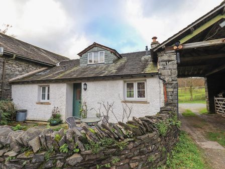 A small white cottage with green door behind a stone wall with chairs and a table at Janes Cottage in Hawkshead