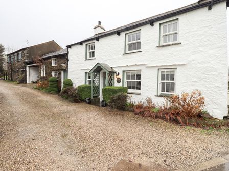A gravel driveway in front of a white cottage with green window frames and trimmed bushes at Nurses Cottage in Hawkshead