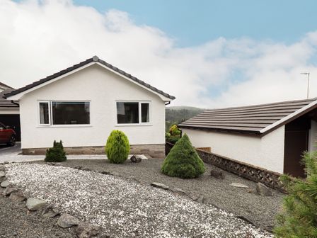 A white house with two windows and shrubs in a gravel garden at Swirl How in Ambleside