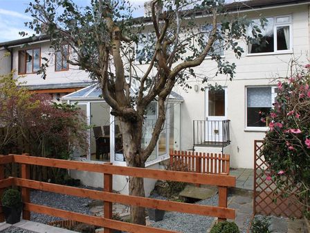 A backyard garden with a tree a wooden fence a conservatory and a white two-story house at Little Brook in Ambleside