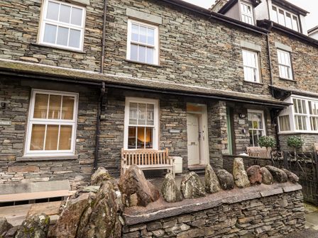 Stone exterior of a building with white windows a wooden bench a stone wall and an open door at Hazeldene Ambleside