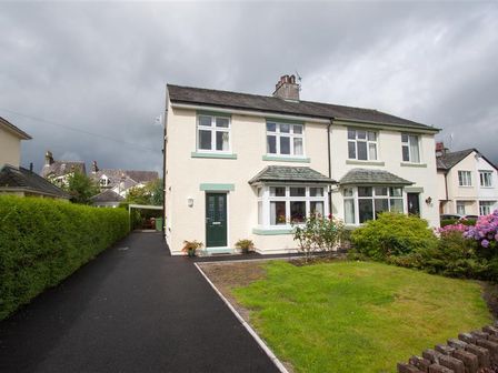 A semi detached house with a green door a driveway and a garden with bushes and flowers at Fell End in Keswick